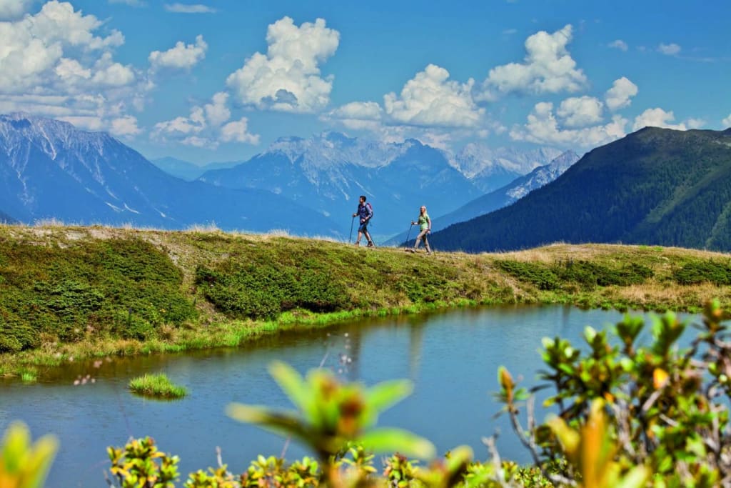 Aktivurlaub für Erlebnissammler - 5 Nächte Zwei Wanderer am Bergsee mit Alpen und blauem Himmel im Hintergrund
