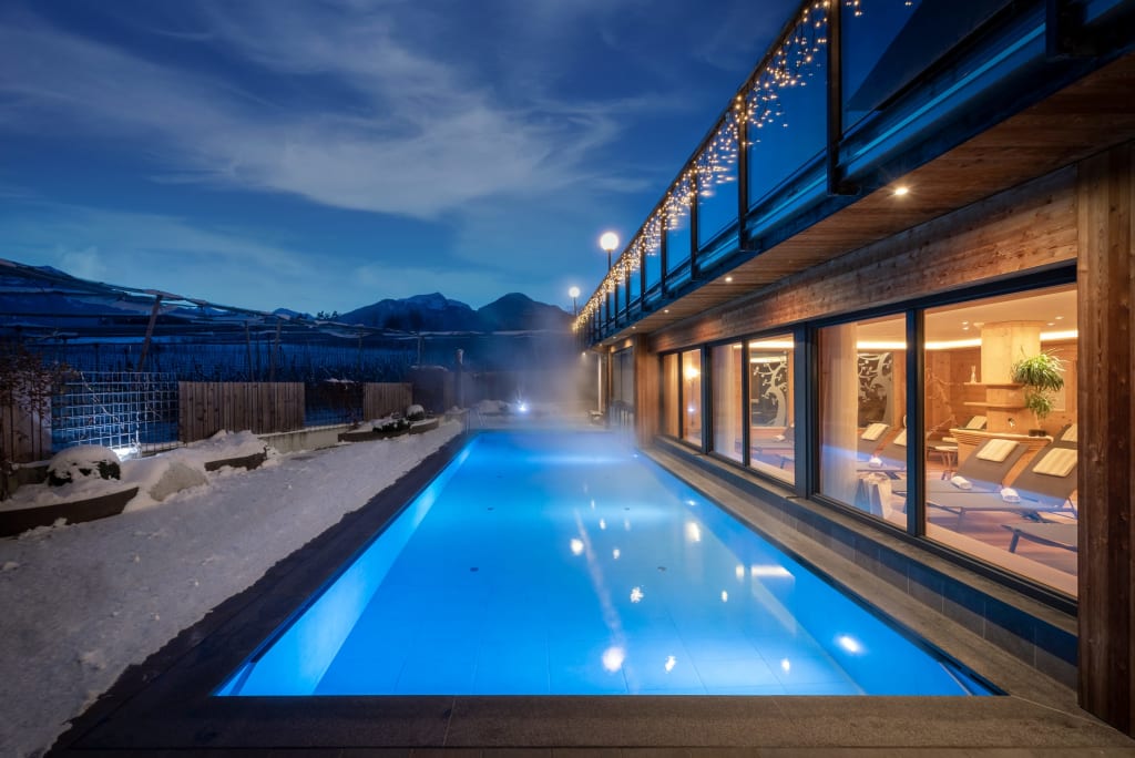 Beheiztes Außenpool bei Nacht neben einem modernen Spa mit Bergblick